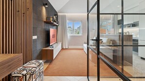 A modern living room with a TV, a sofa, and a glass partition leading to a kitchen. - GuestReady - Stylish base steps from attractions (Porto)