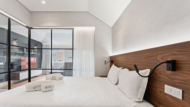 A modern hotel room with a large bed, a wooden headboard, and a view through a glass door to an outdoor area. - GuestReady - Stylish base steps from attractions (Porto)