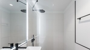 A modern bathroom with a glass shower enclosure, a white sink, and a large mirror. - GuestReady - Stylish base steps from attractions (Porto)