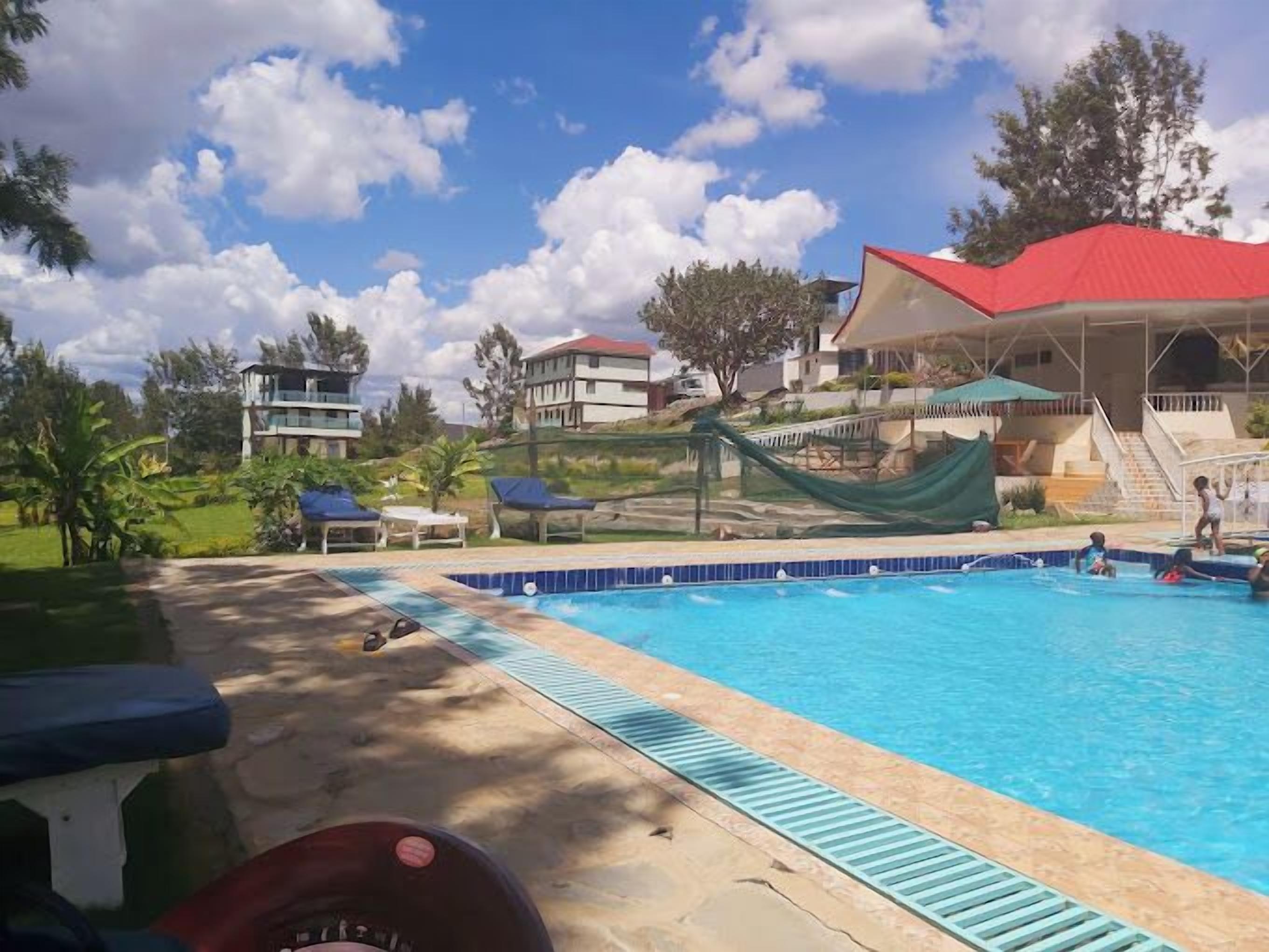 A swimming pool with a blue border, lounge chairs, and a covered area with a red roof.