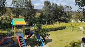 A playground with slides and a climbing structure, surrounded by trees and grass. - The Mugumo Valley Resort (Thika)