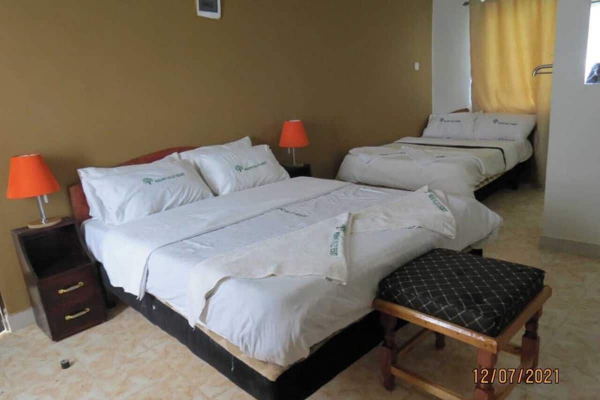 A hotel room with two beds, a wooden bench, and a nightstand with a lamp.