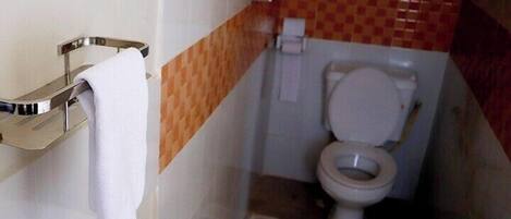 Un baño con un lavamanos blanco, un perchero, un inodoro e interruptor de luz en la pared.