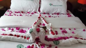 A neatly made bed with white linens and pink flower petals arranged in a decorative pattern. - The Mugumo Valley Resort (Thika)