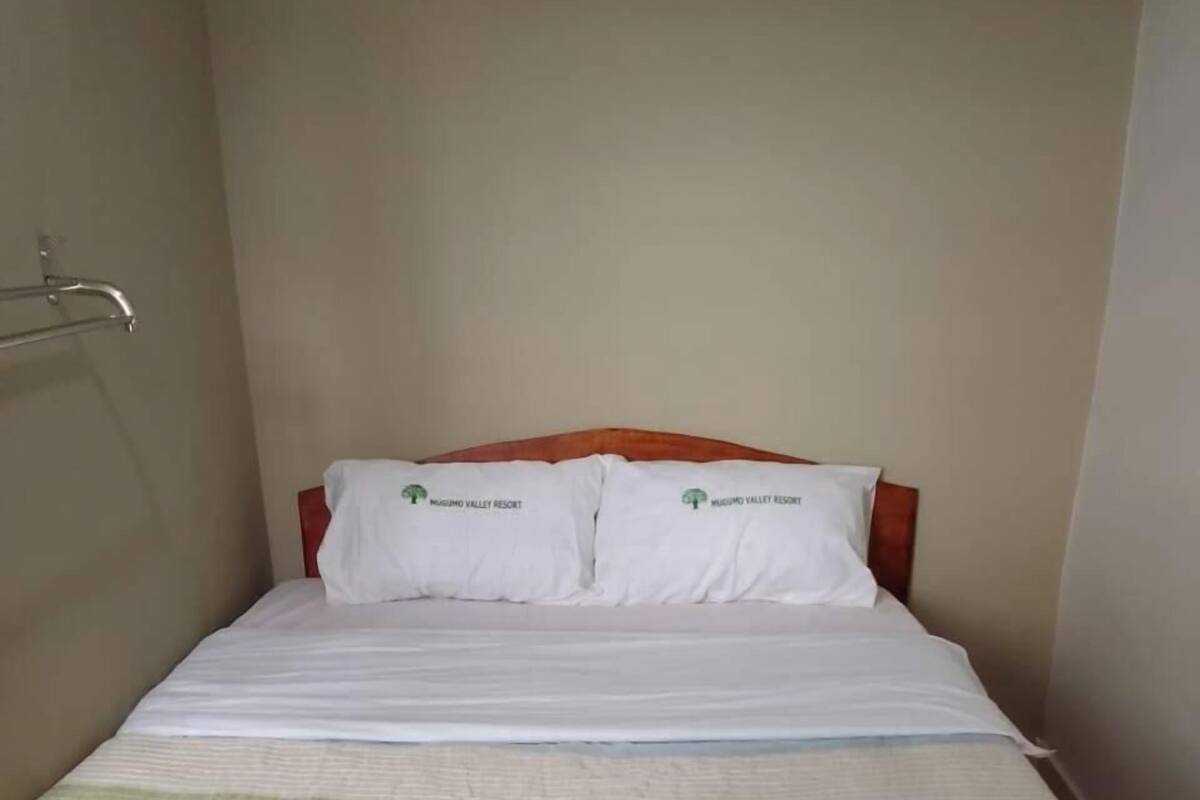 A single bed with a wooden headboard, white bedding, and a logo on the pillows.