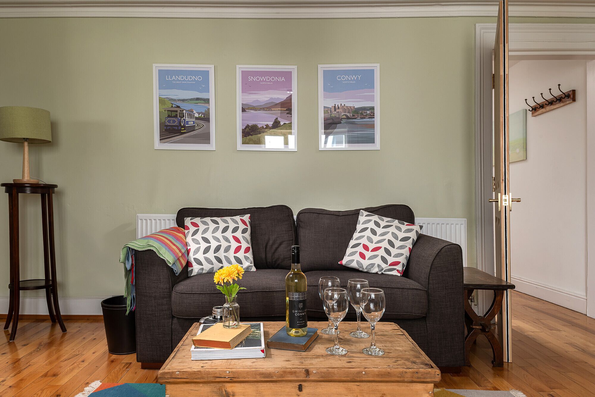 Un salon comprenant un canapé, une table basse avec un livre et des verres à vin, une lampe et trois tableaux encadrés accrochés au mur.