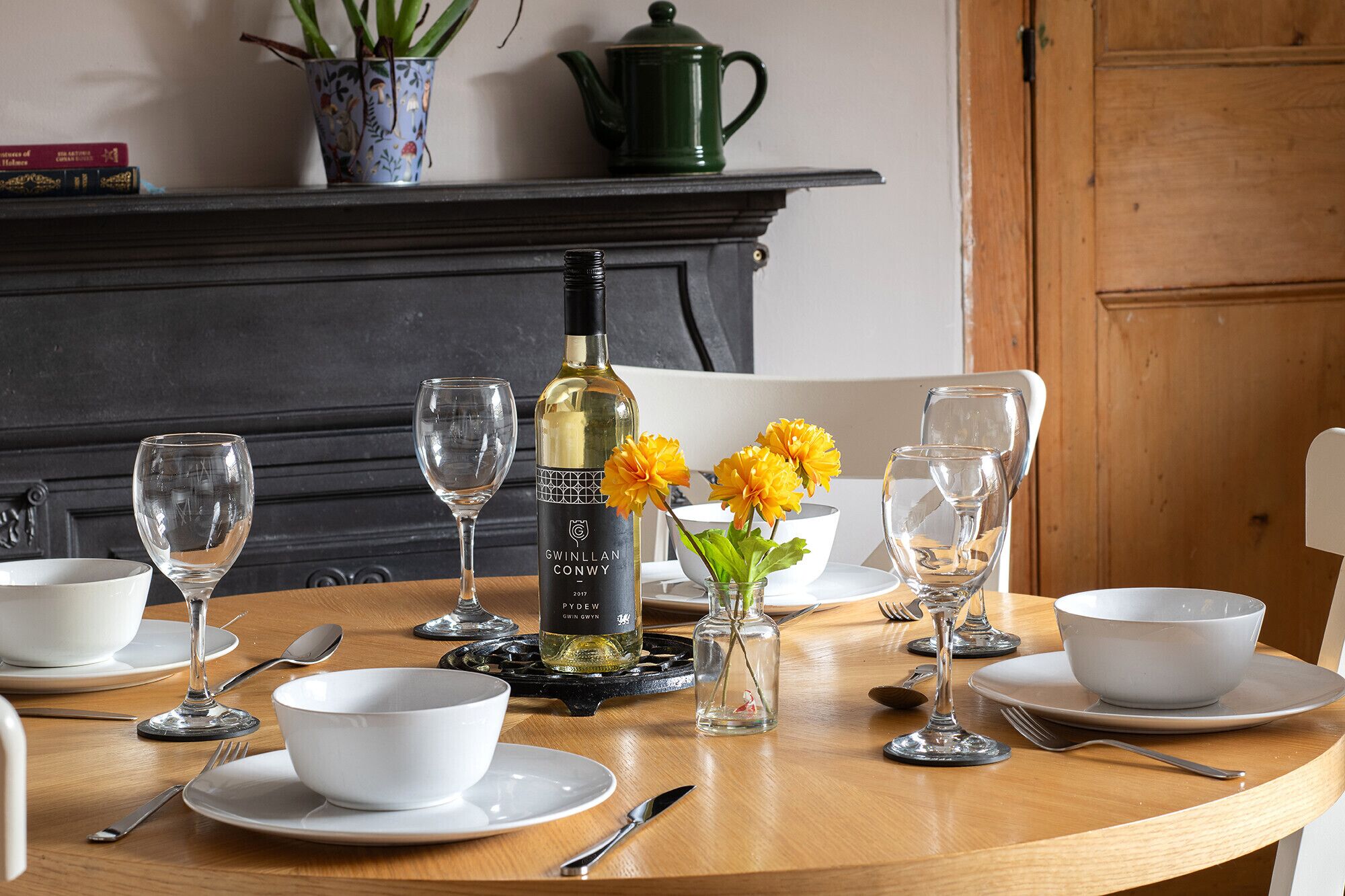 Een eettafel gedekt met witte borden, wijnglazen en een fles wijn.