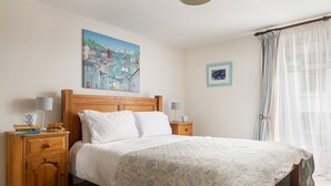 Ein Schlafzimmer mit einem hölzernen Bett, zwei Nachttischen, einem Bild an der Wand und einem Fenster mit Vorhängen.