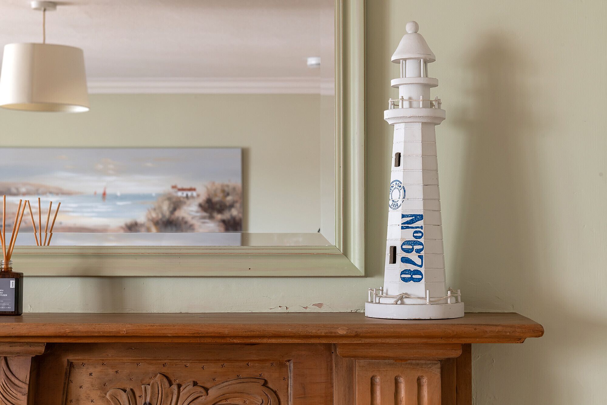 A white lighthouse model with blue text on a wooden mantelpiece.