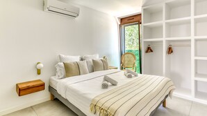 Une chambre à coucher comprenant un lit, une table de chevet, un climatiseur fixé au mur, une fenêtre donnant sur un espace verdoyant et une armoire intégrée.