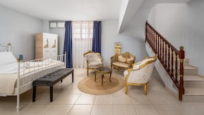 A bedroom with a bed, bedside table, bench, two armchairs, a round coffee table, and a staircase.
