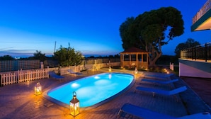 A swimming pool with lounge chairs and lanterns, surrounded by a fence and trees.