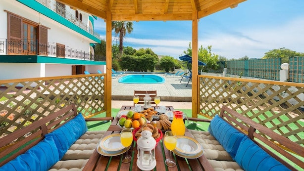 A covered outdoor seating area with a pool in the background.