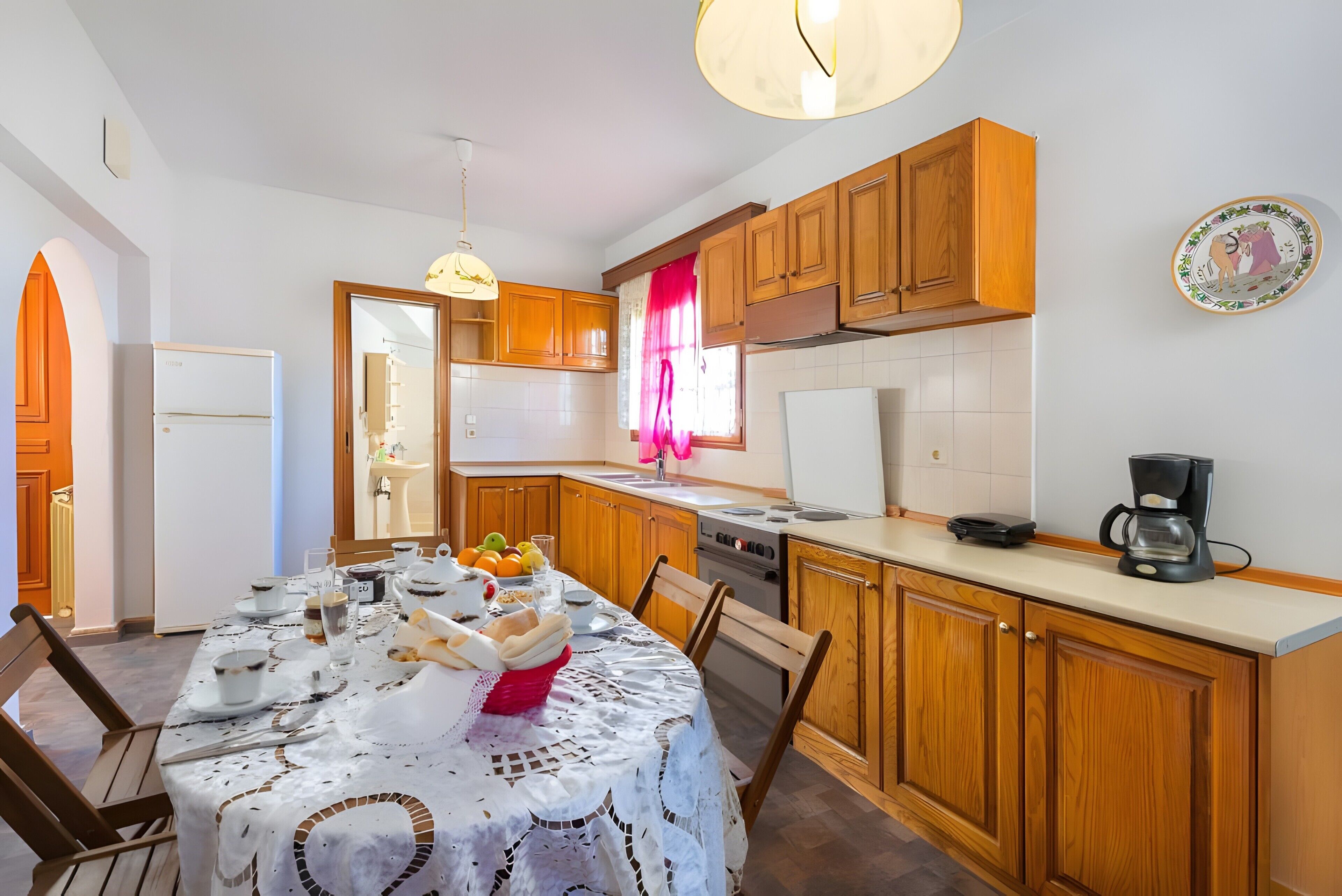A kitchen with wooden cabinets, a dining table set with plates, glasses, and a fruit bowl.