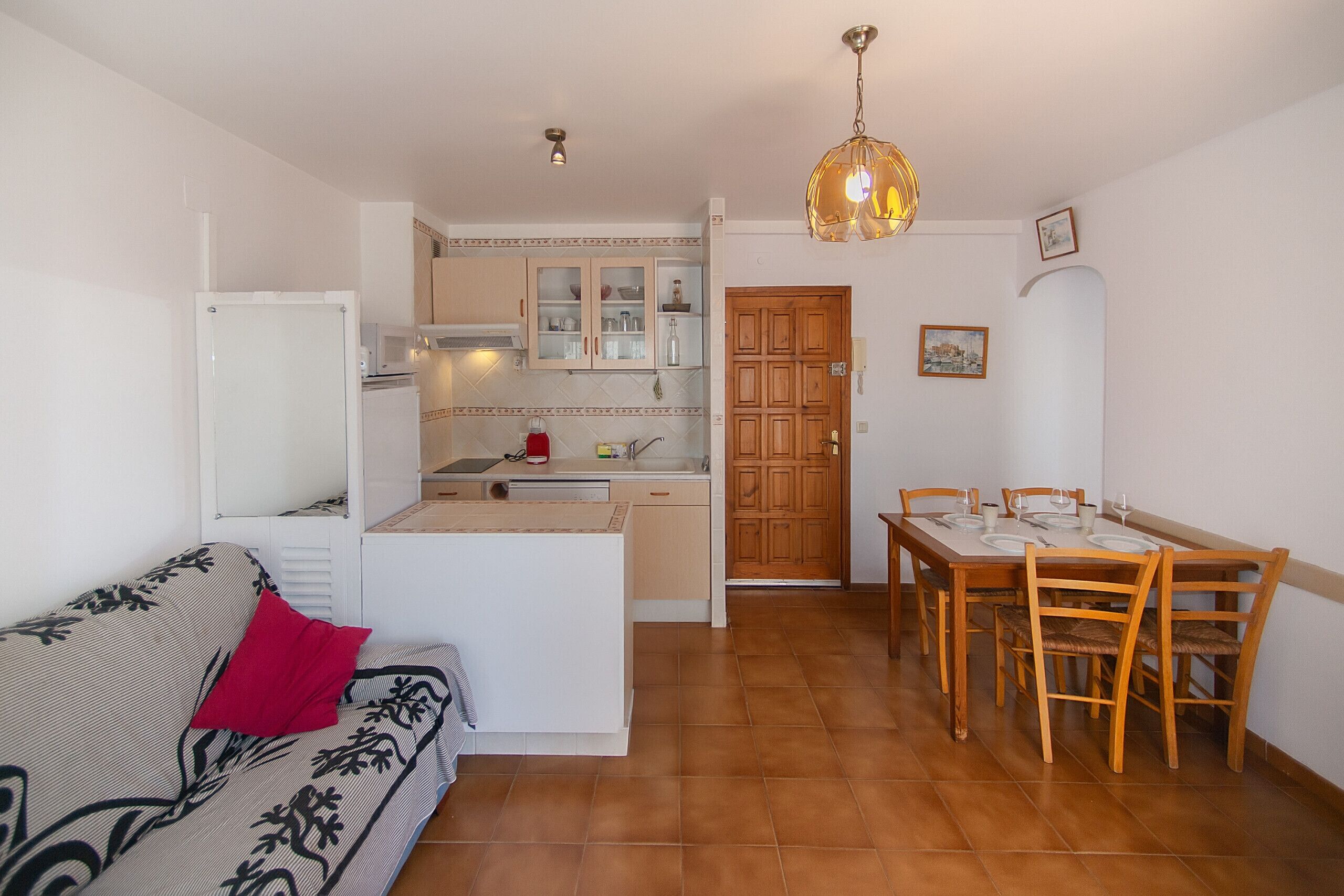 Een knus woongedeelte met een kitchenette, een eethoek en een bank met een rood kussen.