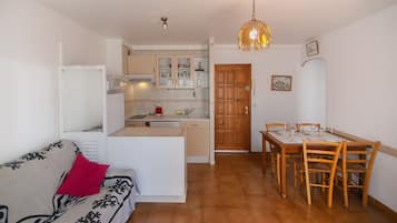 Een knus woongedeelte met een kitchenette, een eethoek en een bank met een rood kussen.