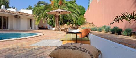 A poolside area with a lounge chair, a table, and a large decorative pillow.