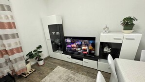 A modern living room with a flat-screen TV, a white cabinet, a potted plant, and a striped curtain.