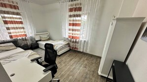 A hotel room with two single beds, a desk, a chair, and a wardrobe.