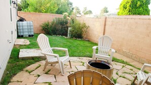 A patio area with a stone floor, white Adirondack chairs, a fire pit, and a small table.