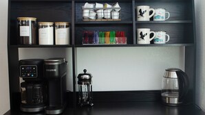 A coffee station with a Keurig coffee maker, a French press, and a coffee grinder on a black countertop.