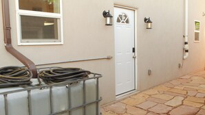 A hallway with a white door, two wall-mounted lanterns, and a metal railing with hoses.