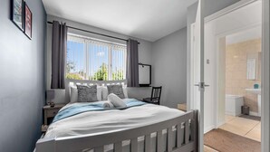 Un dormitorio con cama, mesita de noche, ventana con cortinas, silla y vista al exterior.