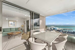 A balcony with a dining table and chairs, a sofa, and a view of the marina and water. - The Penthouse Pad (Mount Maunganui)