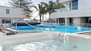 En swimmingpool med et boblebad, omgivet af moderne bygninger og palmer.