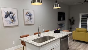 Una cocina moderna con encimera de granito, pileta de acero inoxidable y una zona de comedor con sofá amarillo.