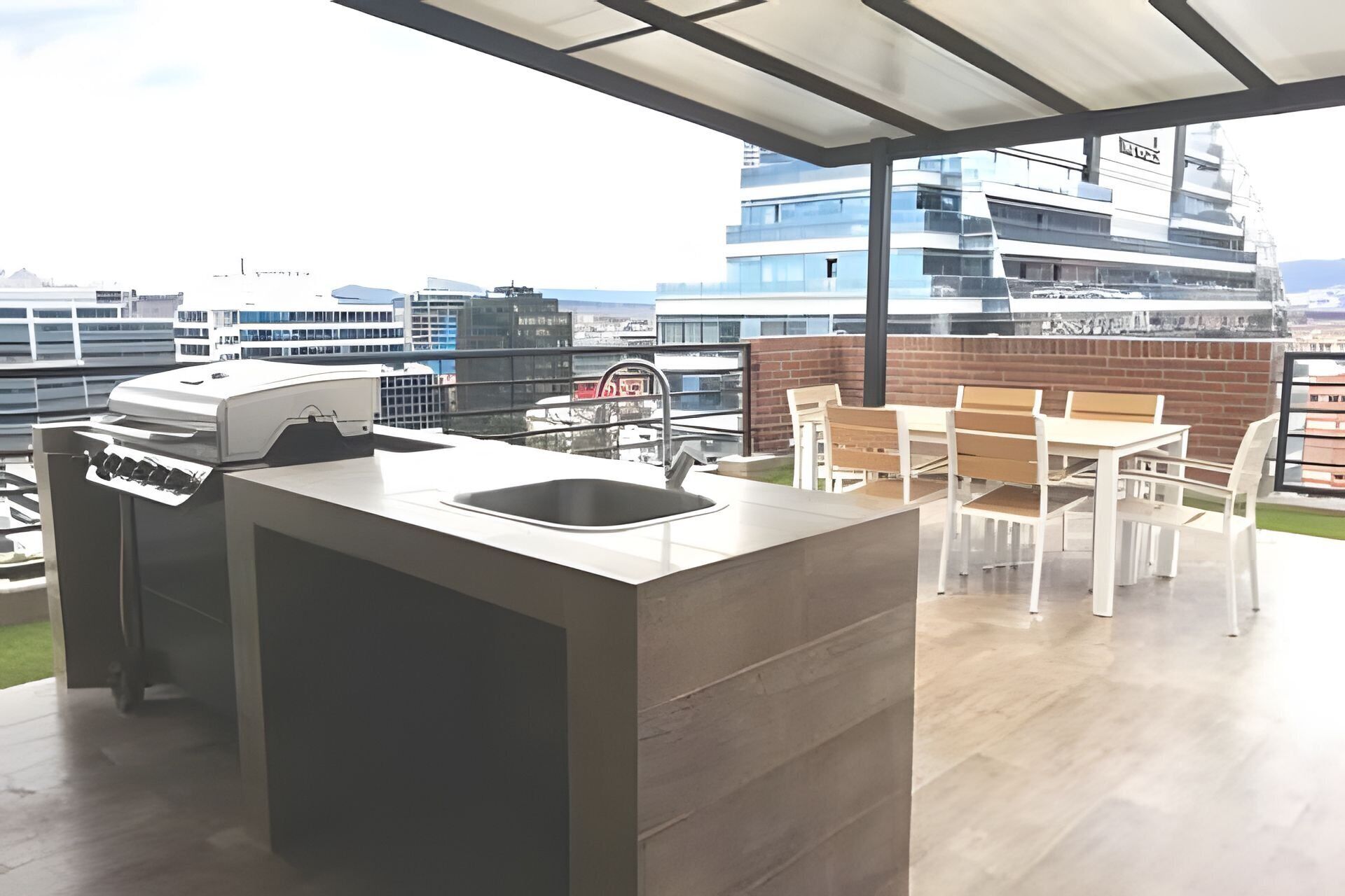 An outdoor kitchen with a grill, sink, and dining area with chairs and a table.