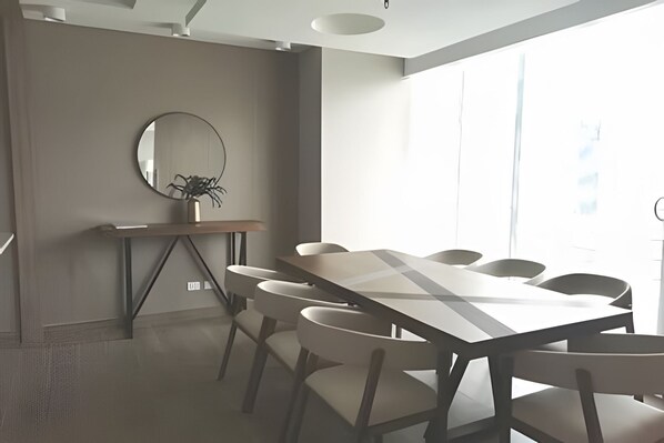 Une salle de conférence avec une longue table, six chaises, un grand miroir rond et une plante en pot.