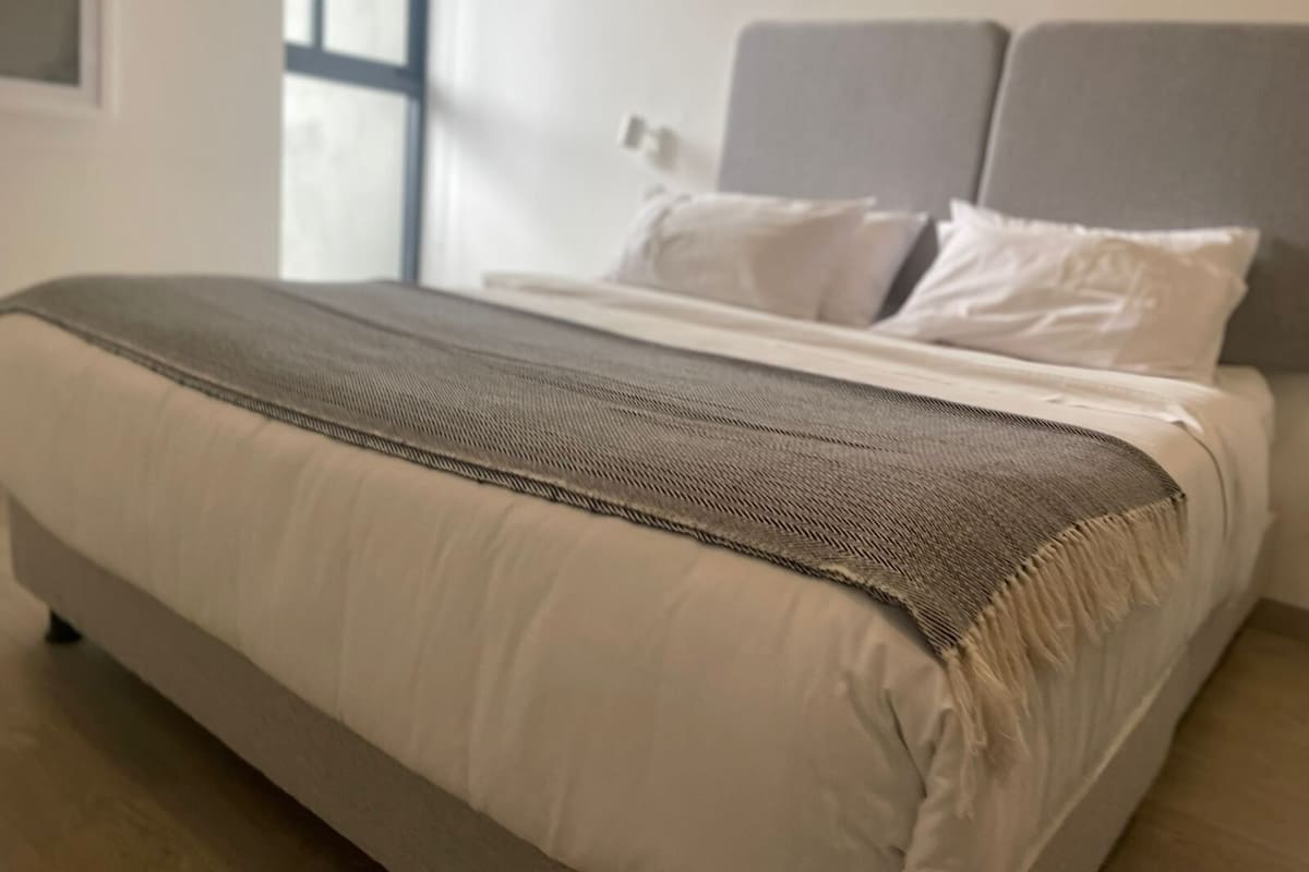A bed with a grey headboard, white pillows, and a beige blanket.