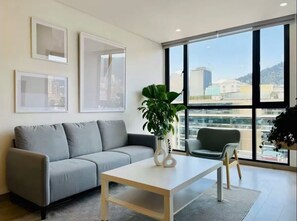 Un salon moderne avec un canapé gris, une table basse blanche et une grande fenêtre donnant sur la ville.