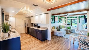A modern kitchen with dark cabinets, a large island, and a dining area with a white table and wicker chairs. - Waterfront Oasis with Boat Lift & Hot Tub in Bokeelia (Bokeelia)