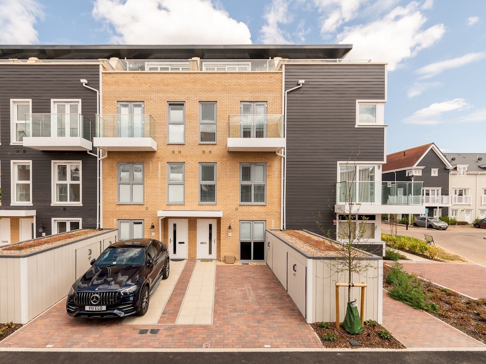 Ein modernes Apartmenthaus mit einer zentralen Eingangshalle, einem Auto auf der Auffahrt und einem kleinen Garten.