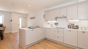 A modern kitchen with white cabinetry, a central island, and a dining area with wooden chairs. - Modern 4BR New Home near Biz Park & Station | Pass the Keys (Reading)