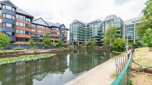 A modern building complex with a river in front, featuring a mix of brick and glass facades. - Stylish Central 1-Bed Flat with Private Balcony | Pass the Keys (Reading)
