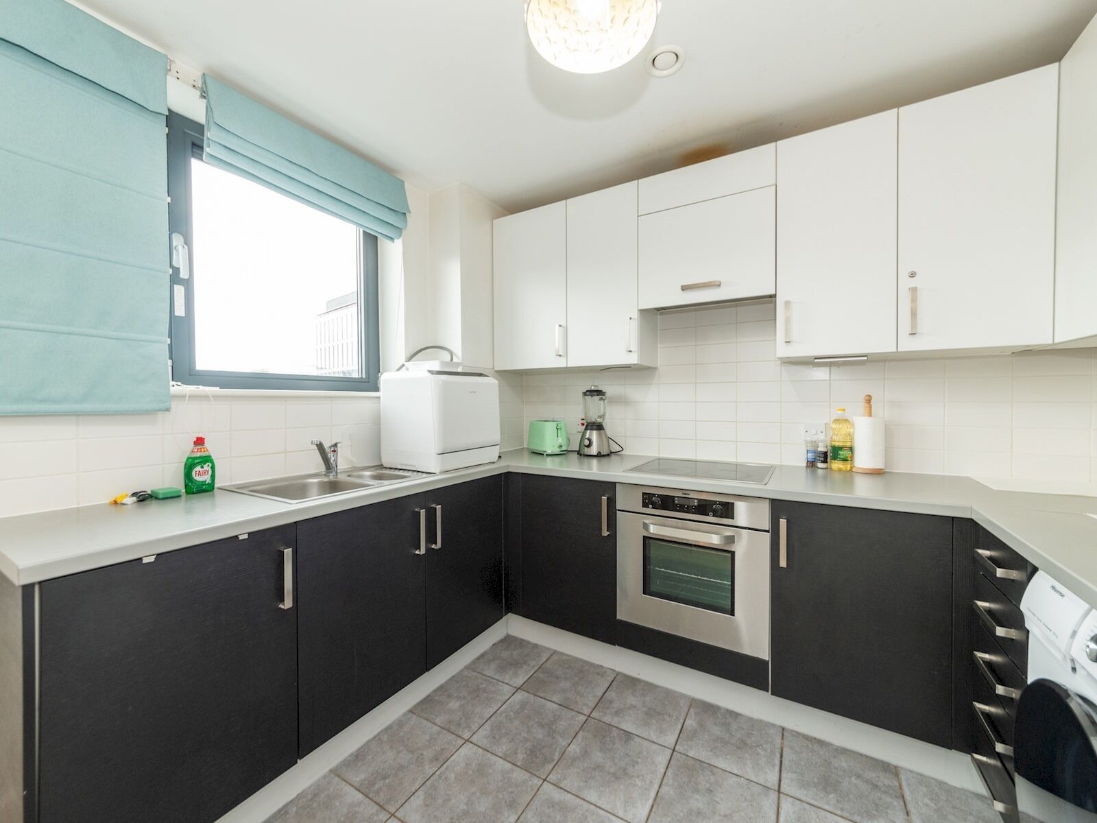 A modern kitchen with dark cabinets, a built-in oven, a sink, and a window with blue curtains.