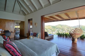 Ein geräumiges Schlafzimmer mit einem großen Bett, einem Holztisch und Blick auf eine gebirgige Landschaft durch eine offene Tür.