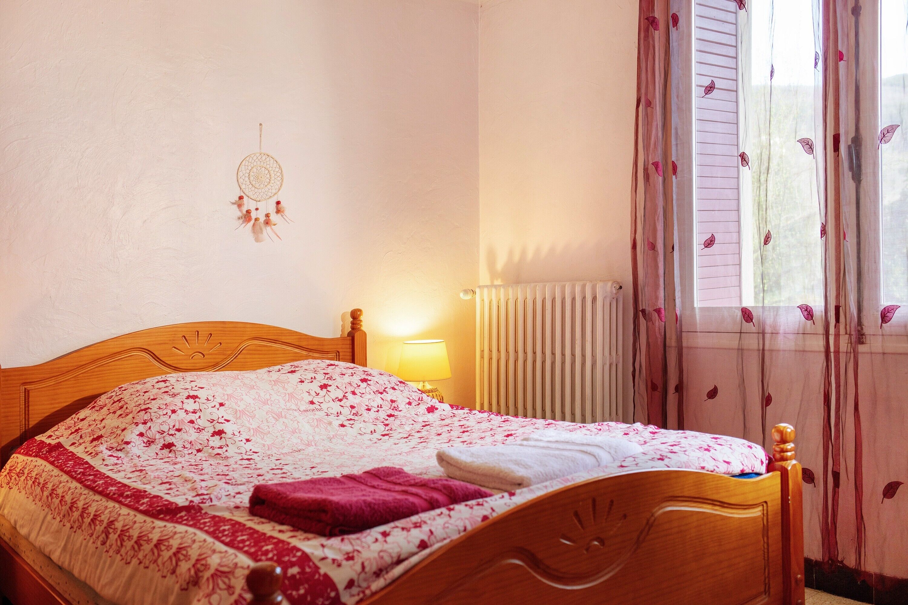 A neatly made bed with a floral bedspread, a bedside lamp, and a dreamcatcher on the wall.