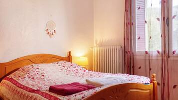 A neatly made bed with a floral bedspread, a bedside lamp, and a dreamcatcher on the wall.