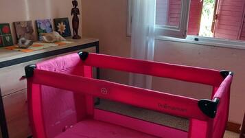 Un berceau rose dans une chambre avec une fenêtre, une commode et des décorations murales.