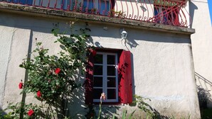 Ein Gebäude mit Balkon, einem kleinen Fenster mit roten Fensterläden und einem Blumenkasten mit roten Blumen.