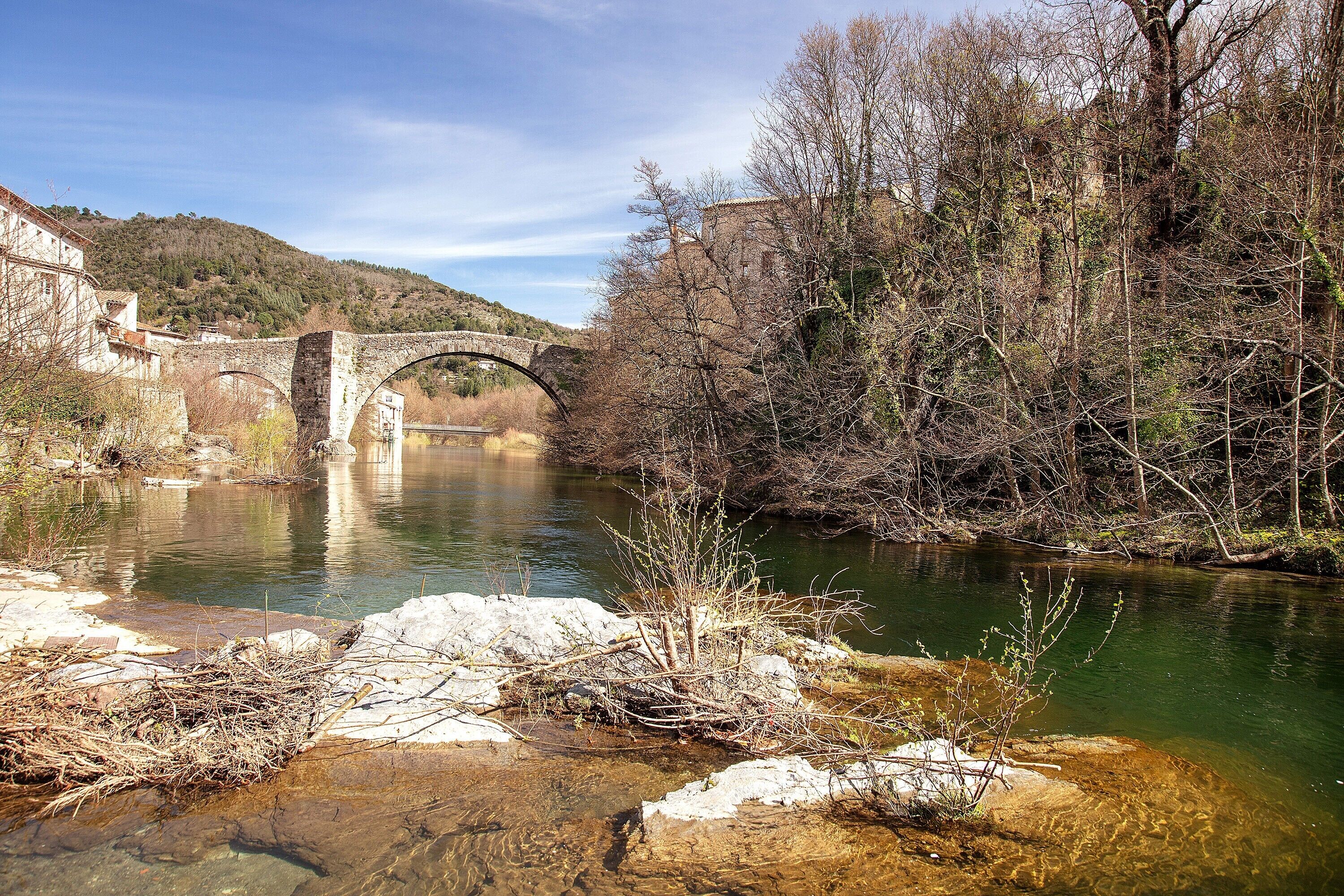 Eine Steinbrücke über einem Fluss, umgeben von Bäumen und einem Gebäude.