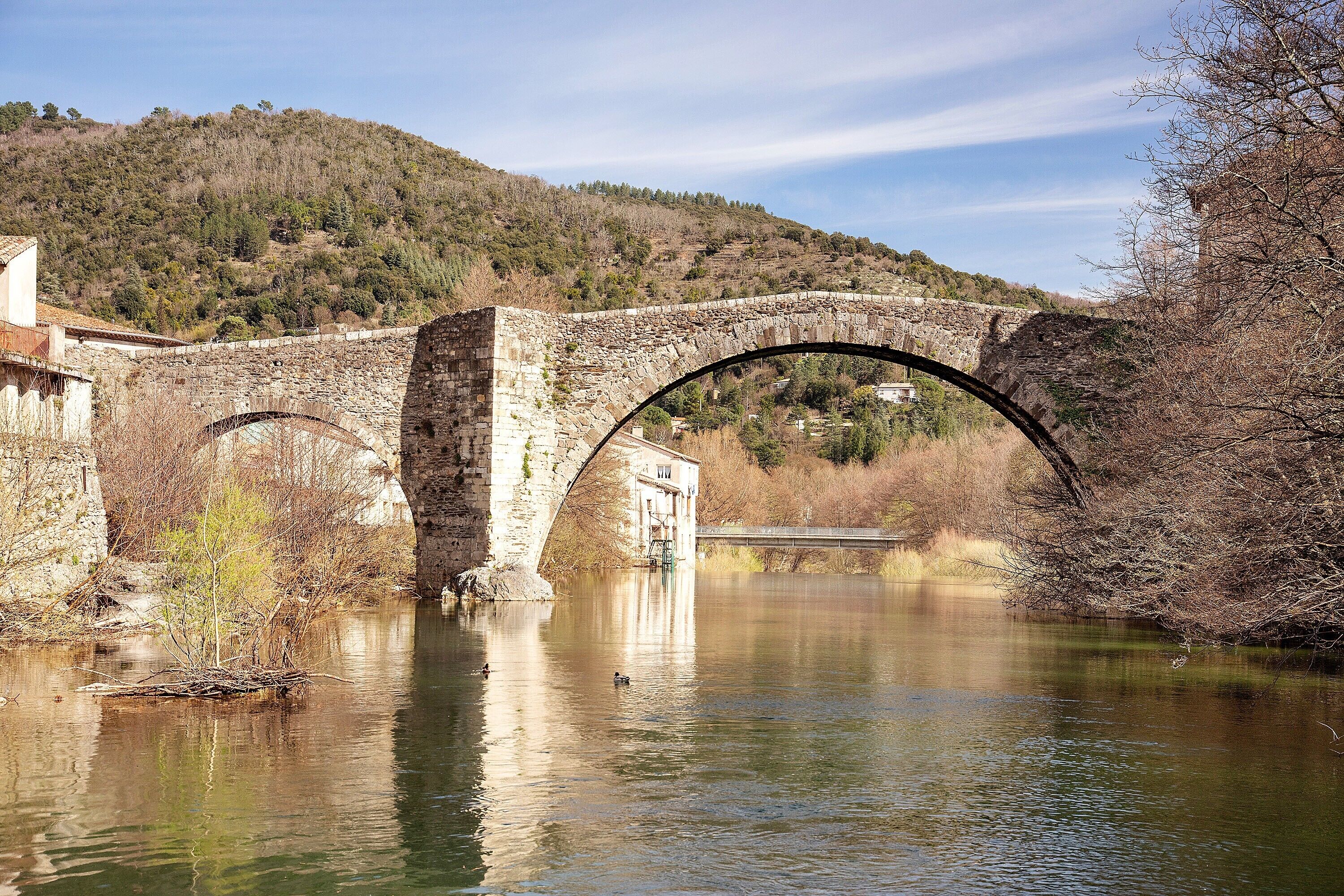 Eine Steinbrücke über einem Fluss, im Hintergrund ein bewaldeter Hang.