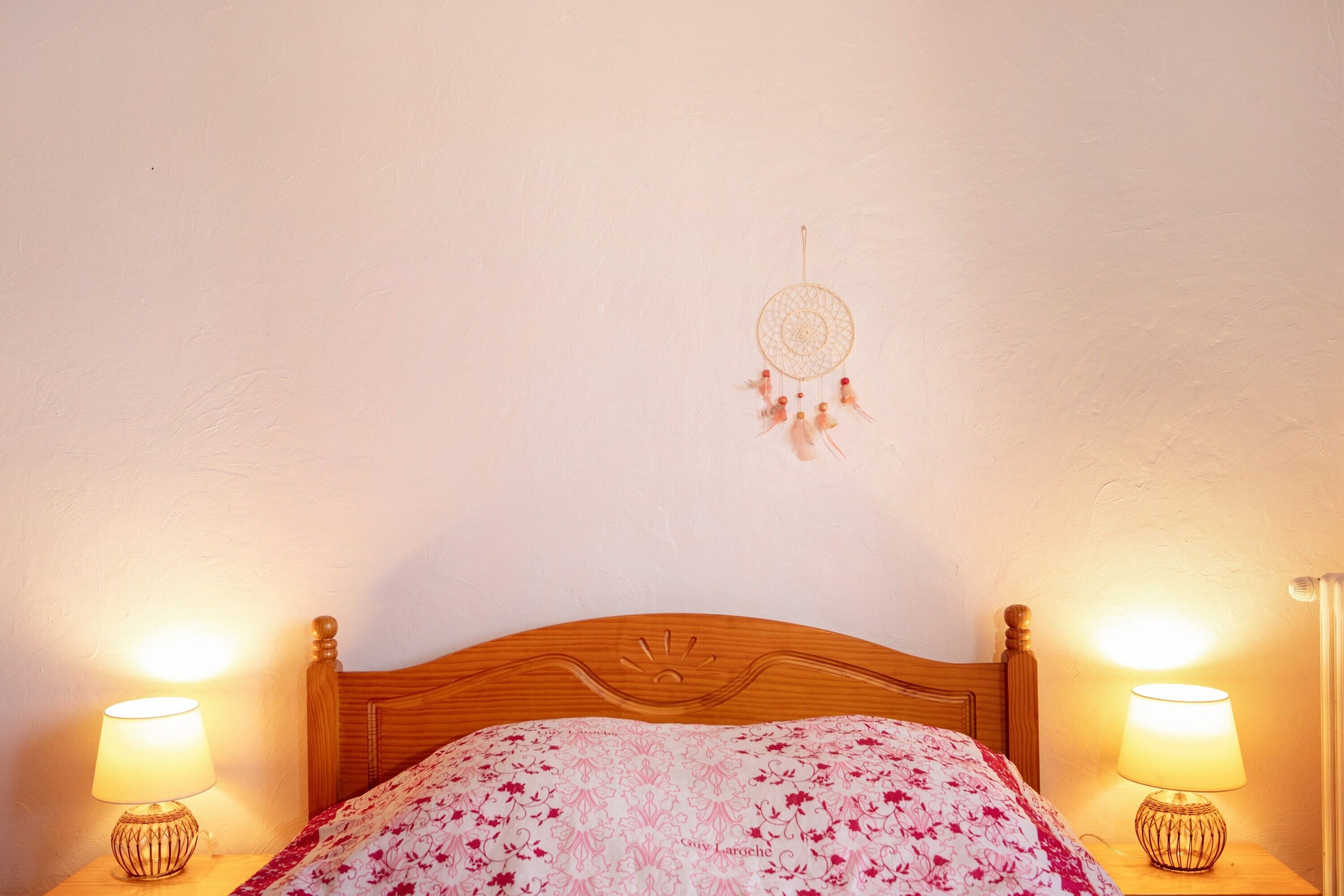 Una cama con una colcha de estampado floral, dos lámparas de noche y un atrapasueños en la pared.