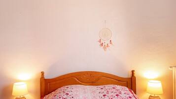 Una cama con una colcha de estampado floral, dos lámparas de noche y un atrapasueños en la pared.