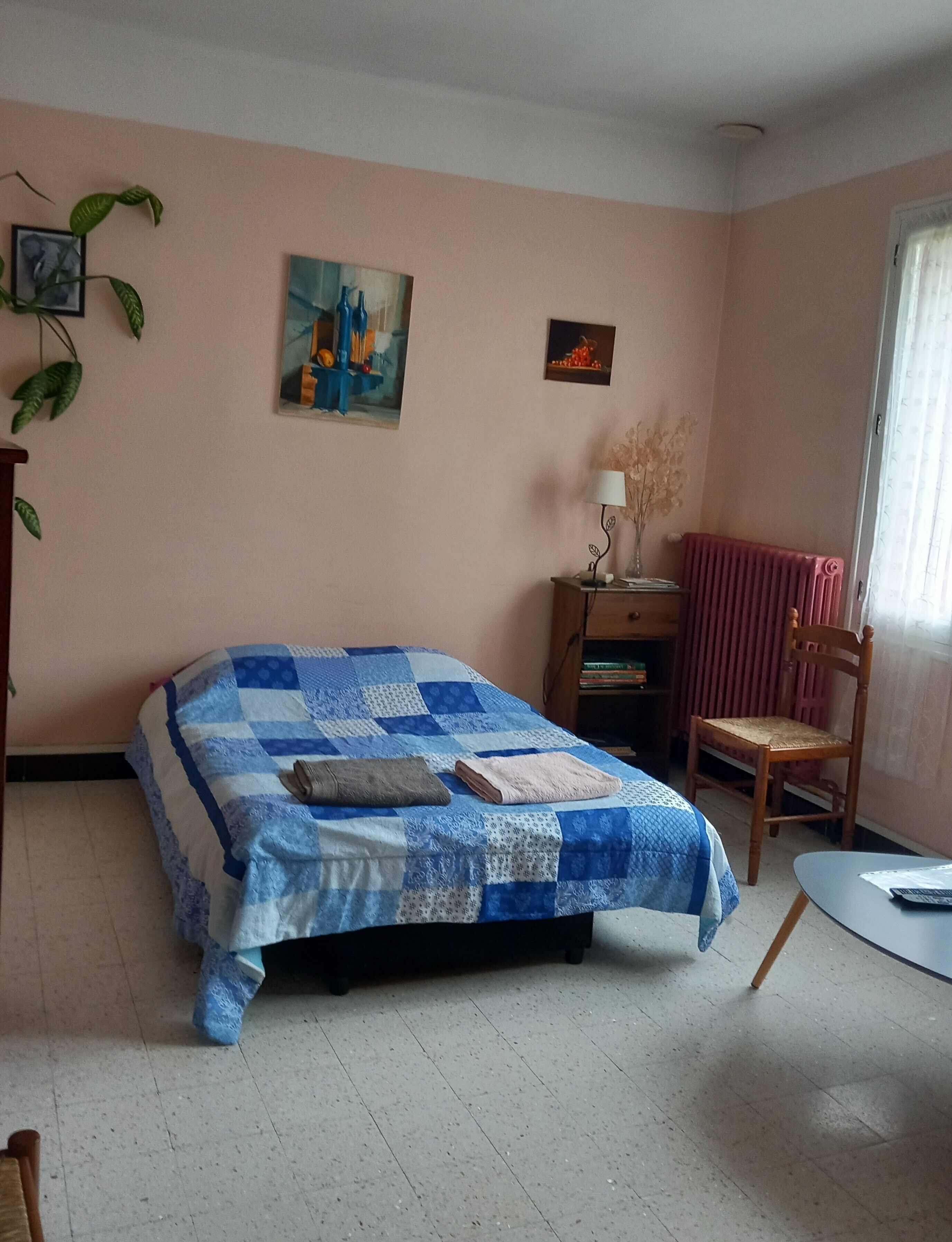 Ein Schlafzimmer mit einem Bett, einem Sessel, einem Heizkörper, einer Lampe und Wanddekorationen.