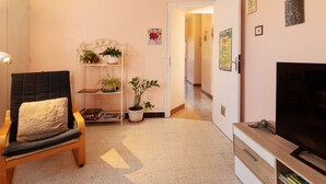 Ein Wohnzimmer mit Fernseher, einem Sessel, einem Bücherregal und einer Zimmerpflanze.